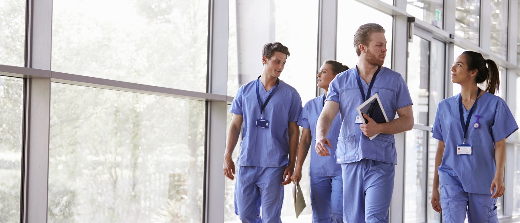 Four healthcare workers in scrubs walking in corridor